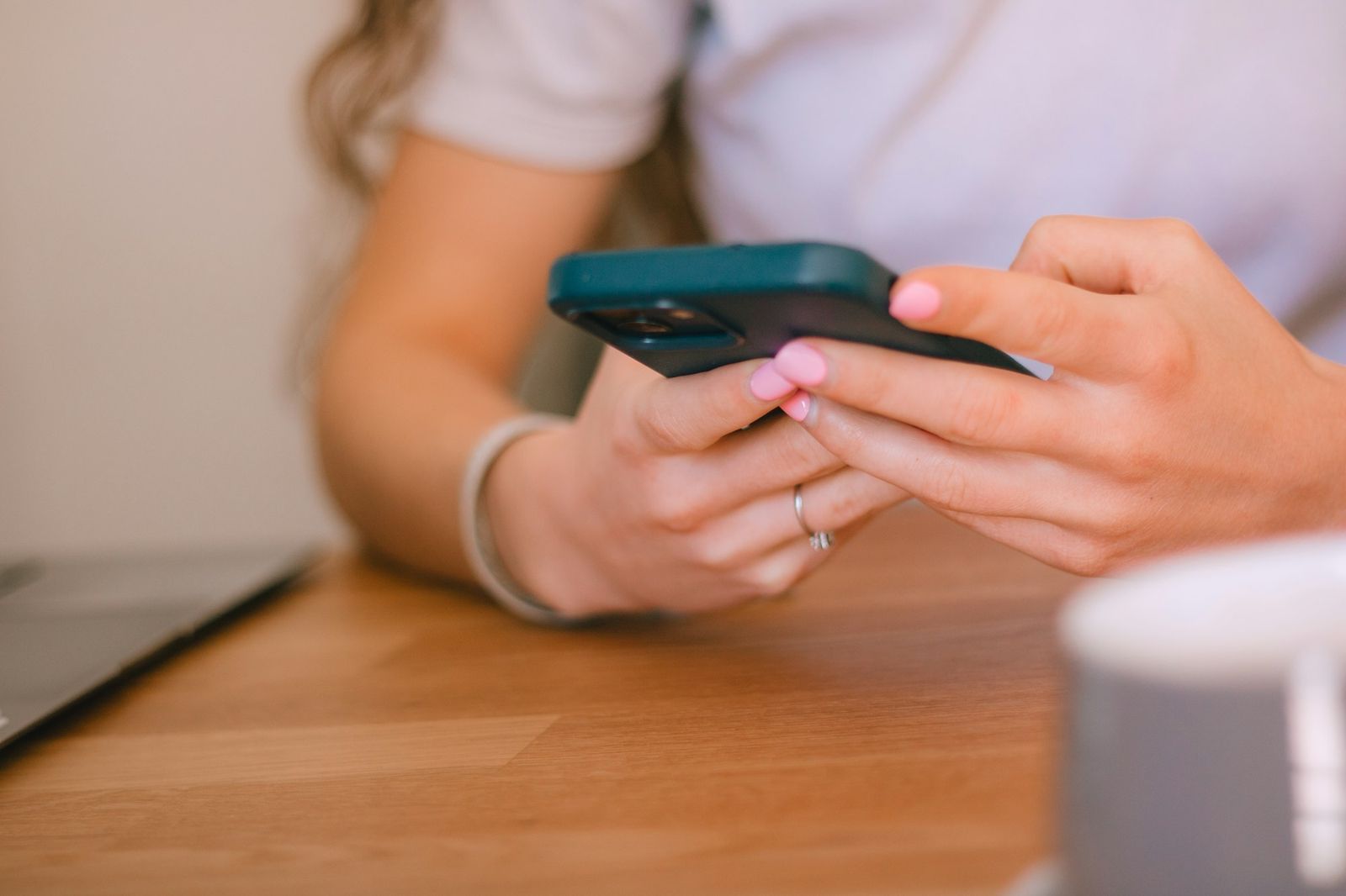 Hands typing a message on a phone at a wooden cafe table