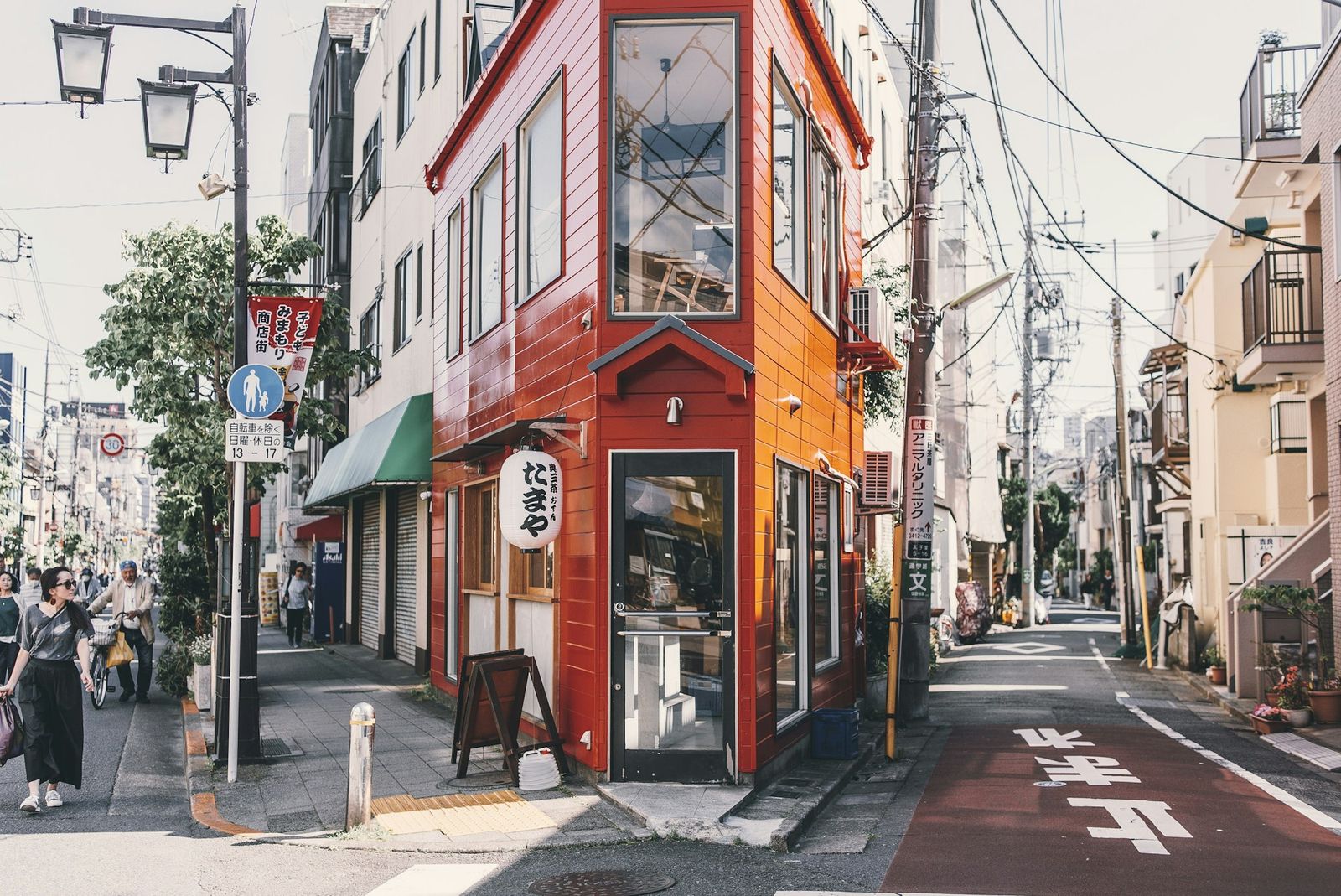 A quiet Japanese side street with a red wooden shopfront on a sunny afternoon