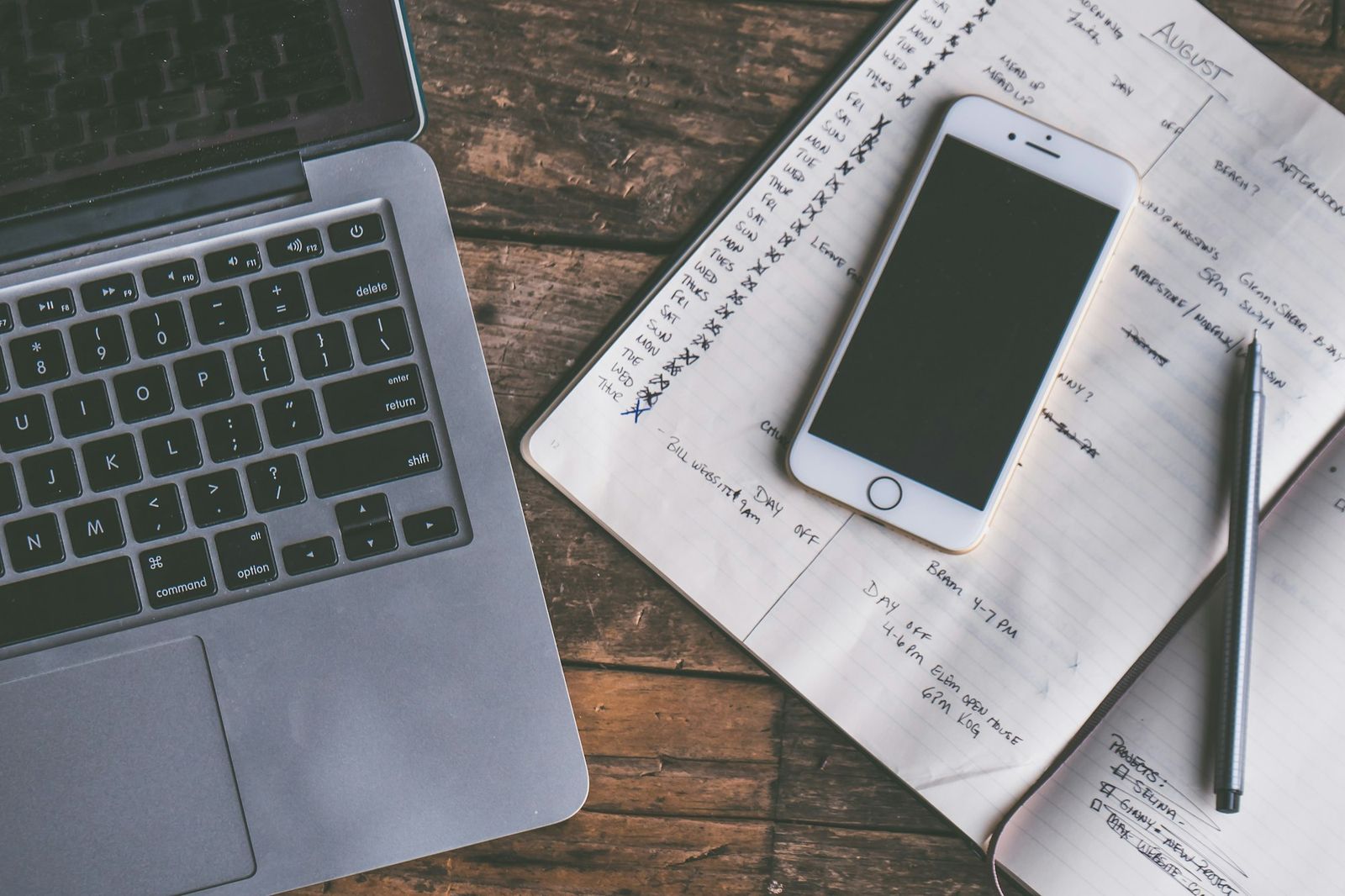 A phone resting on handwritten notes beside a laptop on a wooden desk